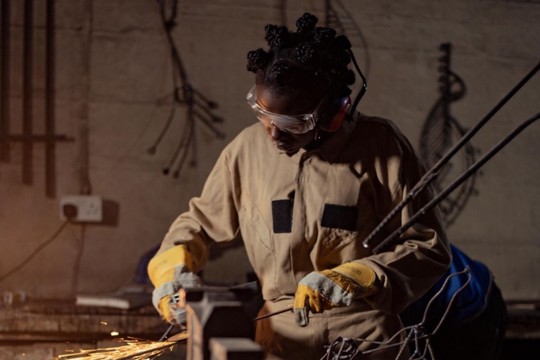Woman fabricator in coveralls and safety glasses grinding steel with sparks